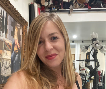 Model on a gold velvt couch wearing Frederick's of Hollywood's Rosalind collection corset and garter belt, both in black lace. 