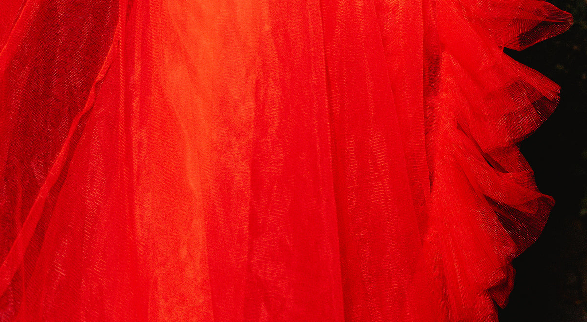 A close-up of a bright red sheer tulle fabric with layered ruffles and a textured mesh backing, shown against a very dark background.
