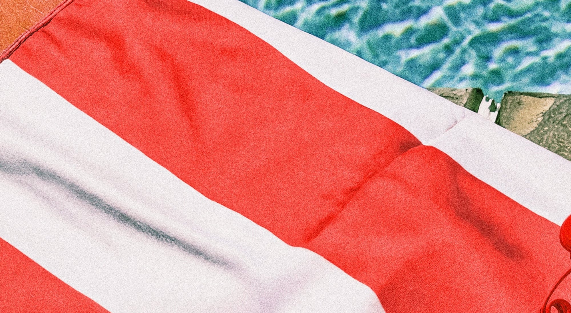 Close-up of a red and white striped towel with a pool in the background