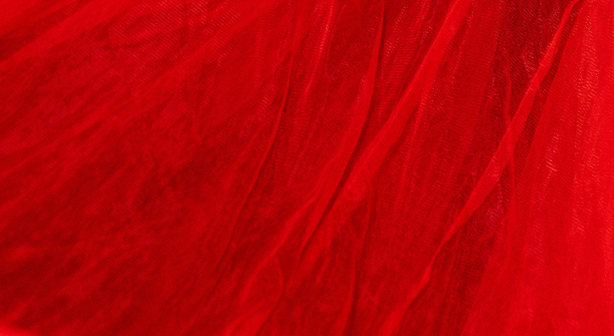 A close-up of bright red sheer mesh or tulle fabric with soft folds and a textured overlay.