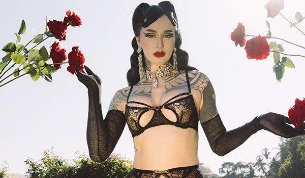 Person wearing a black lace bra and holding red roses against a natural background