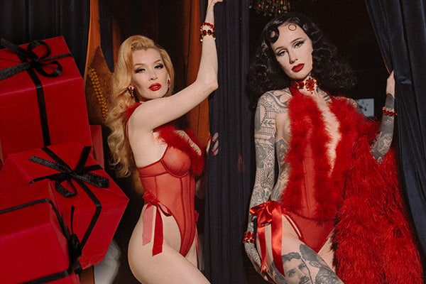 Two women in red outfits posing in front of gift boxes.