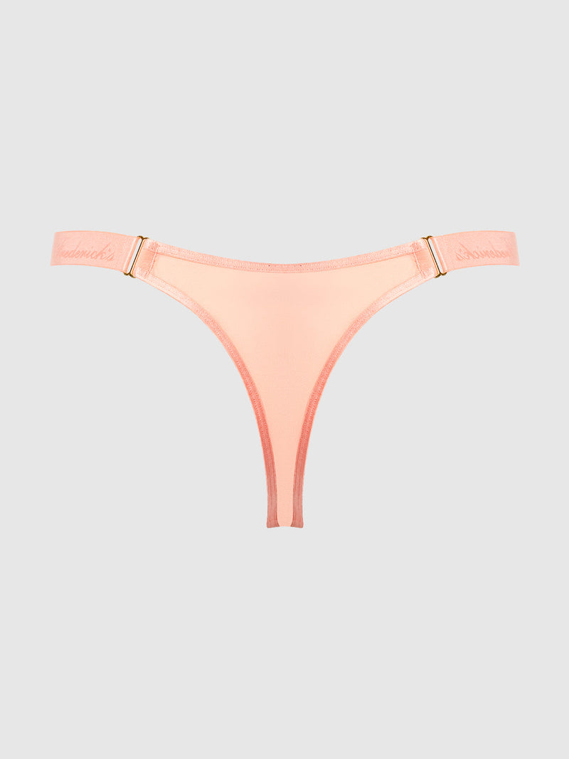 The Pia Elastic Side Mesh Thong by Frederick's of Hollywood features light peach semi-sheer mesh, a thin elastic waistband with gold-tone hardware, and embroidered script on the sides—sexy lingerie styled on a plain gray background.