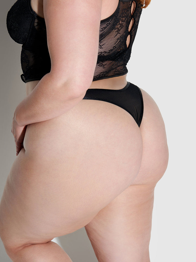 A woman models the Frederick's of Hollywood Chiara Classic Lace Thong, shown from the waist down and turned slightly to the side, standing against a plain background.