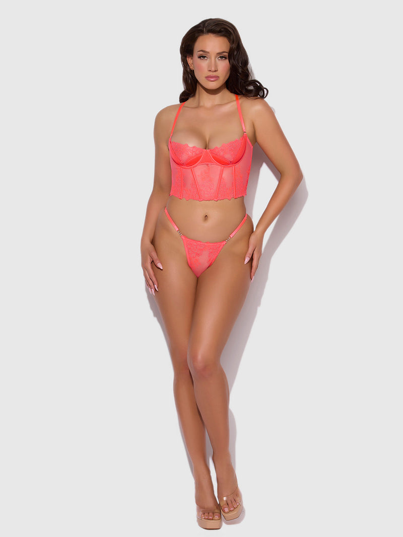 A woman poses against a white background wearing the Frederick's of Hollywood Wren Embroidered Crotchless Thong With Side Sliders in coral pink lace, styled with clear high-heeled sandals.