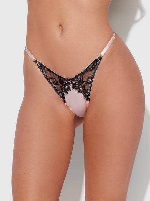 A close-up shows a woman from mid-torso to upper thighs wearing the Frederick's of Hollywood Rising Star Lace & Liquid Satin Thong in light pink with black lace and thin side straps, set against a white background.