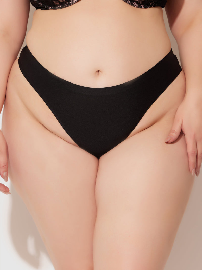 A close-up shot of a plus-size model from torso to upper thighs wearing Frederick's of Hollywood No Show Lasercut Micro Front & Mesh Back Tanga, black underwear designed to prevent panty lines, against a light background.