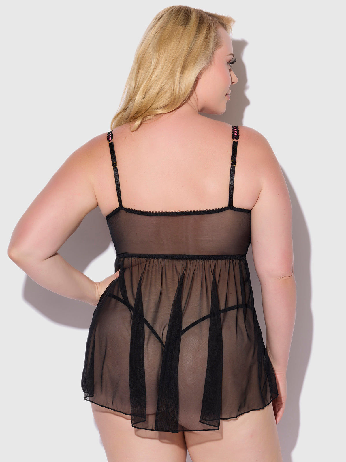 A woman with blonde hair is seen from behind wearing the Frederick's of Hollywood Harlow Embroidered Mesh & Elastic Longline Babydoll, featuring adjustable straps, against a plain light background.