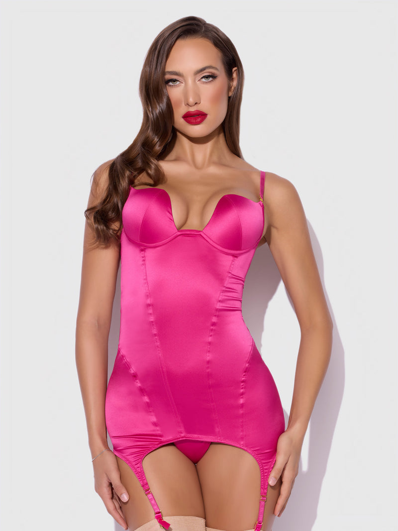 A woman with long brown hair and red lipstick models the Frederick's of Hollywood Rising Star Plunge Open Back Chemise Set in Petra Satin, featuring garter straps, against a plain light gray background.