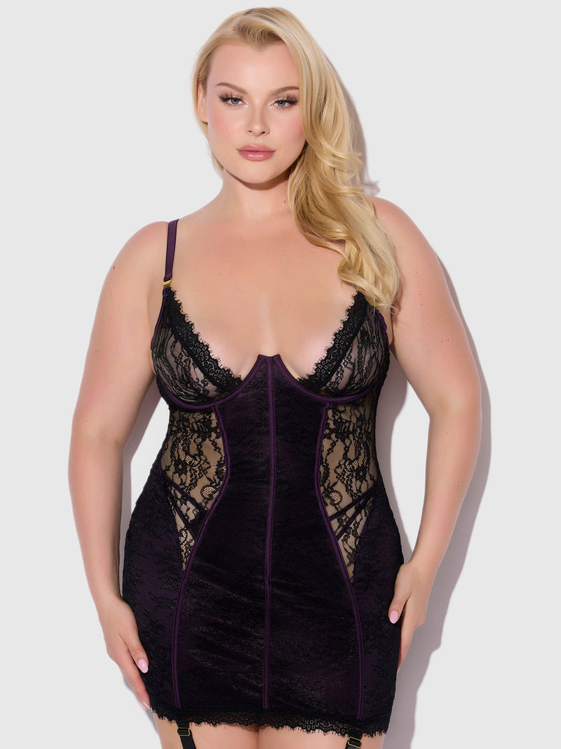 A woman with long blonde hair wears the Frederick's of Hollywood Rosalind Satin & Lace Underwire Chemise, featuring sheer lace panels and adjustable straps, standing against a plain light gray background.