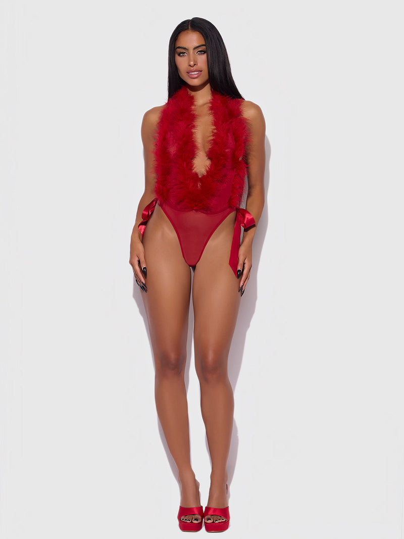 A woman poses against a plain white background wearing the Frederick's of Hollywood Scarlett Plunging Drop Off Marabou Teddy, a red feather-trimmed piece with a deep neckline, high-cut sides, and side-tie accents. She pairs it with red heels and has long straight hair.