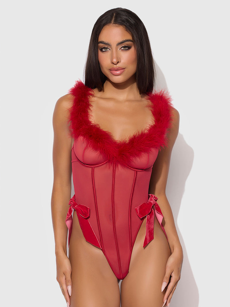 A woman models the Scarlett Marabou & Mesh Teddy by Frederick's of Hollywood, featuring mesh details and red velvet bows at the hips, standing against a light gray background.