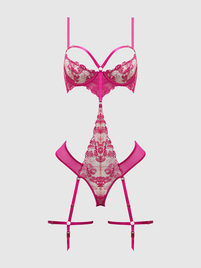 The Venus Lace Strappy & Thigh Gartered Teddy by Frederick's of Hollywood features floral-embroidered, blacklight-friendly lace and sheer mesh details in hot pink, styled with garter straps, shown on a plain white background.