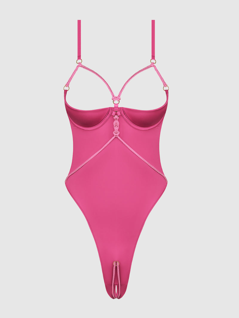 The Nadya Liquid Satin & Rope Crotchless Teddy by Frederick’s of Hollywood is a bright pink strappy bodysuit featuring an open cup design, intricate rope strap details, and a high-cut thong style, shown against a plain white background.