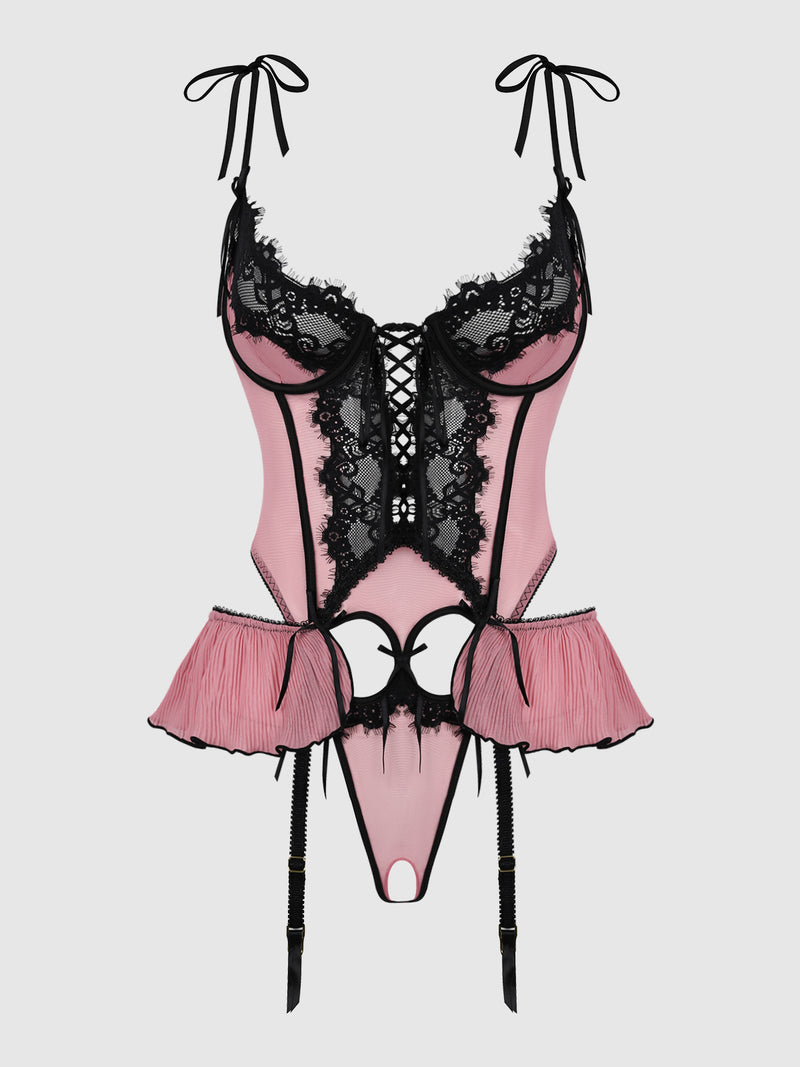 The Esme Chiffon & Lace Crotchless & Open Back Teddy by Frederick’s of Hollywood is a pink and black lace lingerie bodysuit featuring ribbon ties at the shoulders, lacing detail at the front, pleated side panels, and attached garter straps, displayed on a plain light background.