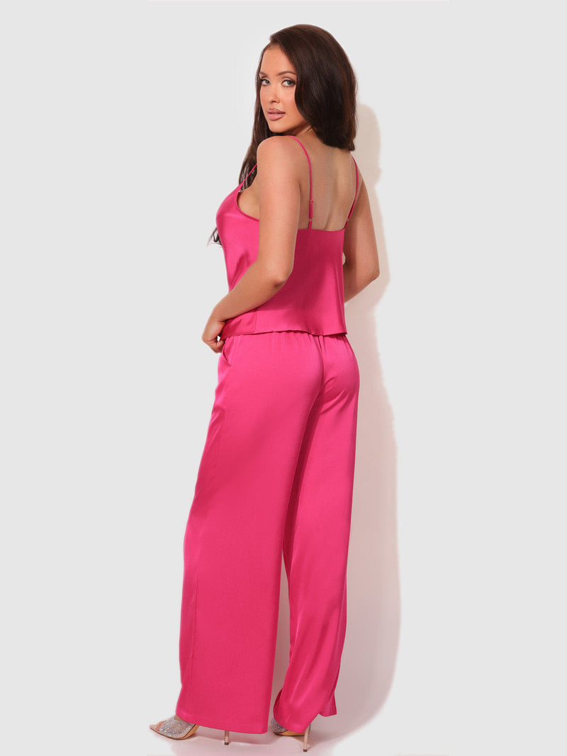 A woman wears a bright pink Billie Satin Draped Cami & Pant Sleep Set consisting of a camisole and matching wide-leg pajama pants.