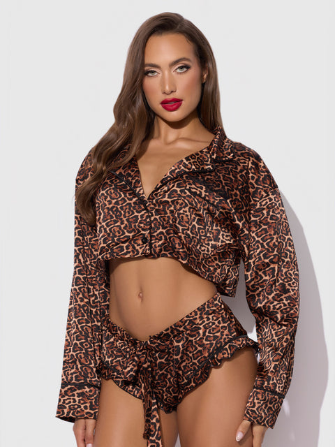 A woman with long brown hair wears the Frederick's of Hollywood Raven Leopard And Lace Sleep Set—a matching ensemble featuring a cropped, long-sleeve leopard-print top and high-waisted shorts—standing against a white background.