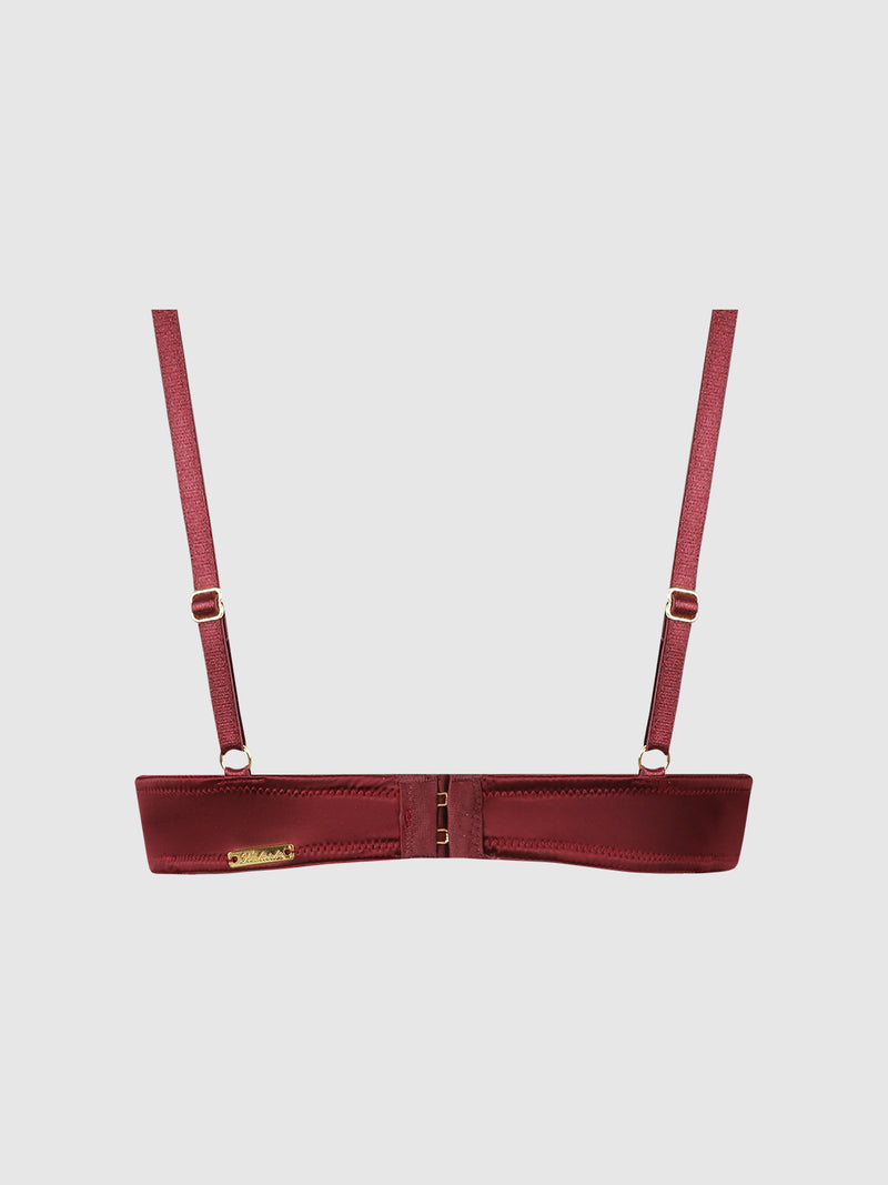A back view of the Frederick’s of Hollywood Emery Liquid Satin & Chain Bra in burgundy satin is shown against a plain light gray background. The bra features adjustable shoulder straps with gold hardware, a gold branded plaque on the left side, and a hook-and-eye closure at the center back.