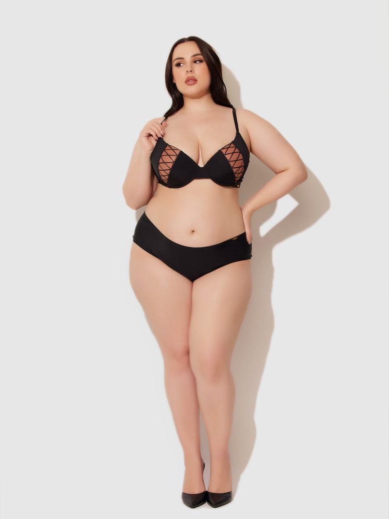 A woman with long dark hair poses confidently in the Frederick's of Hollywood Natalia Micro Lace Up Plunge Push Up Bra and high heels against a plain white background.