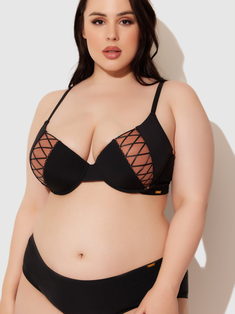 A woman with long dark hair wears the Frederick's of Hollywood Natalia Micro Lace Up Plunge Push Up Bra and matching black underwear, standing against a light background.