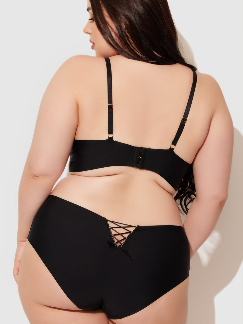 A woman with long dark hair is shown from the back wearing Frederick’s of Hollywood's Natalia Micro Lace Up Plunge Push Up Bra in black, paired with high-waisted lace-up underwear, set against a plain light background.