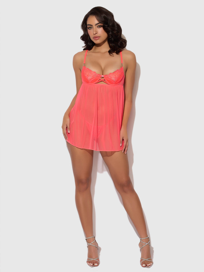 A woman poses against a light gray background, wearing the Wren Satin & Embroidered Tulip Demi Babydoll by Frederick's of Hollywood—sheer bright pink with tulip-shaped cups, lace details, and a flowy silhouette—paired with strappy high heels.