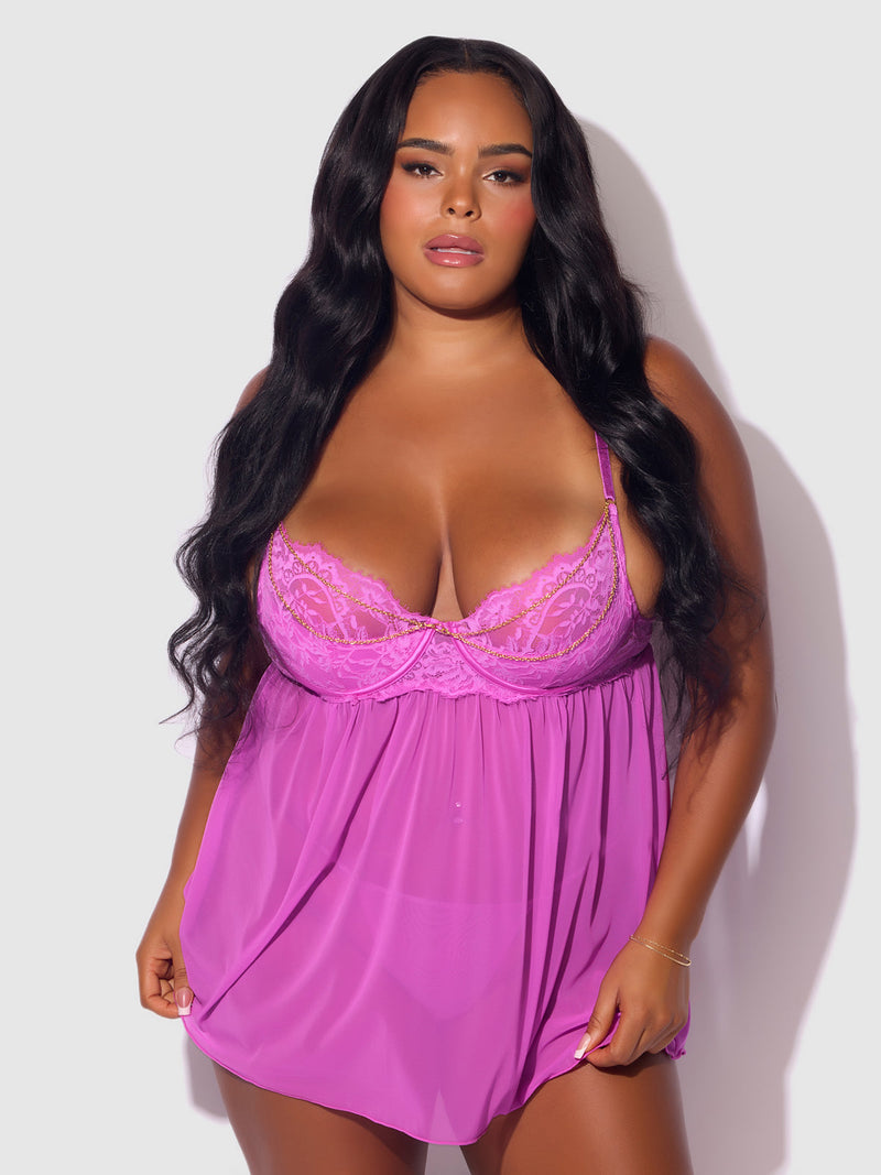 A woman with long wavy hair models the Arianna Lace & Chains Underwire Babydoll Set by Frederick's of Hollywood. She stands against a light background, confidently gazing at the camera.