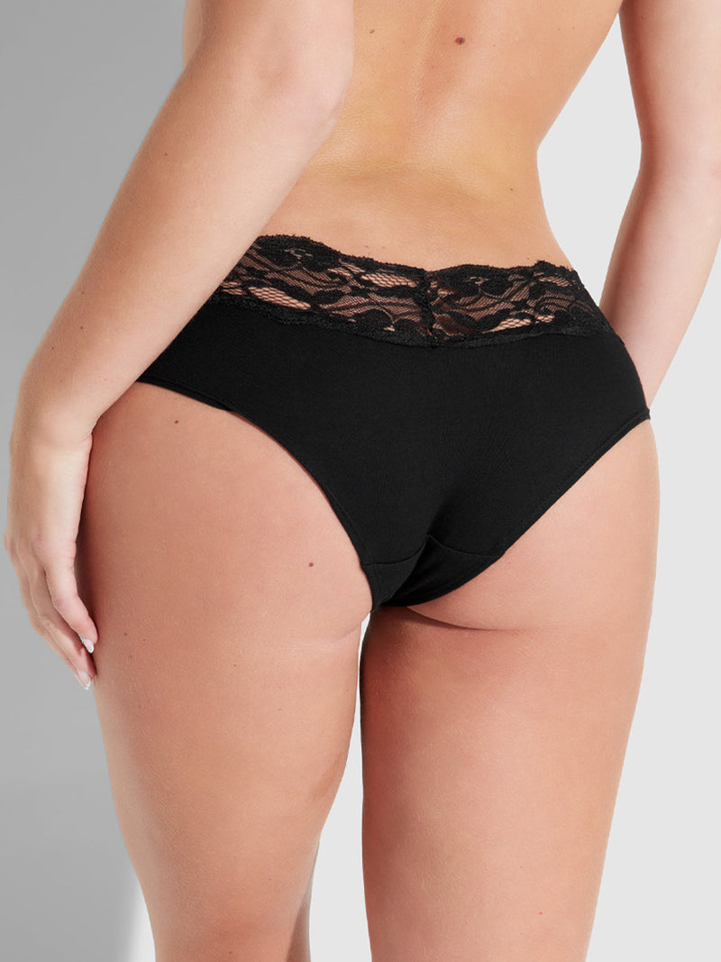 A person shown from the back wears the Bridget Cotton & Lace Hipster by Frederick's of Hollywood—black stretch cotton hipster underwear with lace waistband, displayed against a neutral background for everyday comfort.