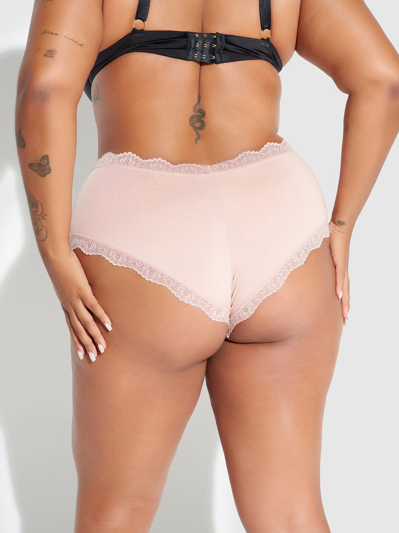 A person with medium brown skin and tattoos on their back, arms, and hip models the Jenna Micro Cheeky panties by Frederick's of Hollywood in pale pink lace, paired with a black bra.