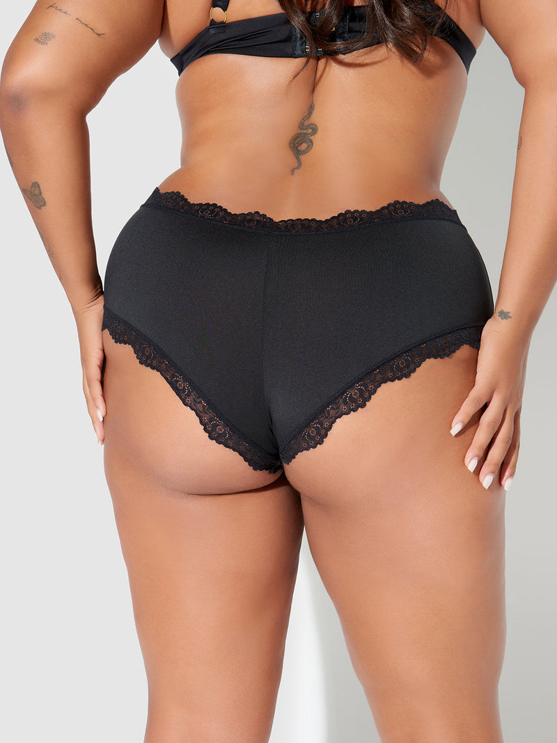 A woman models the Frederick's of Hollywood Jenna Micro Cheeky black lace-trimmed underwear with a matching bra, shown from the back, highlighting her arm and back tattoos.