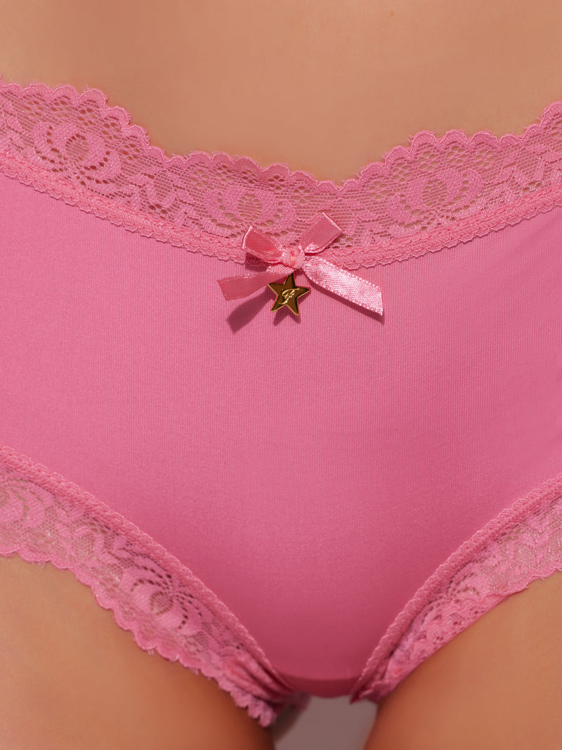 Close-up of a person wearing Frederick's of Hollywood Jenna Micro Cheeky underwear, featuring silky-soft pink fabric with lace trim, a small pink satin bow, and a gold star charm at the center waistband.