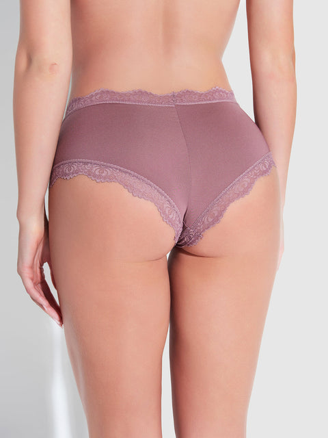 A person is seen from behind wearing Frederick's of Hollywood Jenna Micro Cheeky panties in mauve, featuring medium rise, scalloped lace edges, and a cheeky fit with moderate coverage against a softly lit plain background.