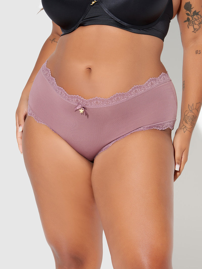 Wearing Frederick's of Hollywood Jenna Micro Cheeky mauve lace panties with a small bow and a cheeky fit, paired with a black bra, the person shows floral tattoos on their arm and thigh.