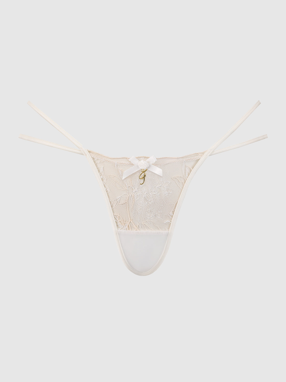 The Delfina Embroidered Backless Cheeky by Frederick's of Hollywood features a cream lace design with thin side straps, a small white bow at the center, and a gold charm beneath, shown against a plain white background.