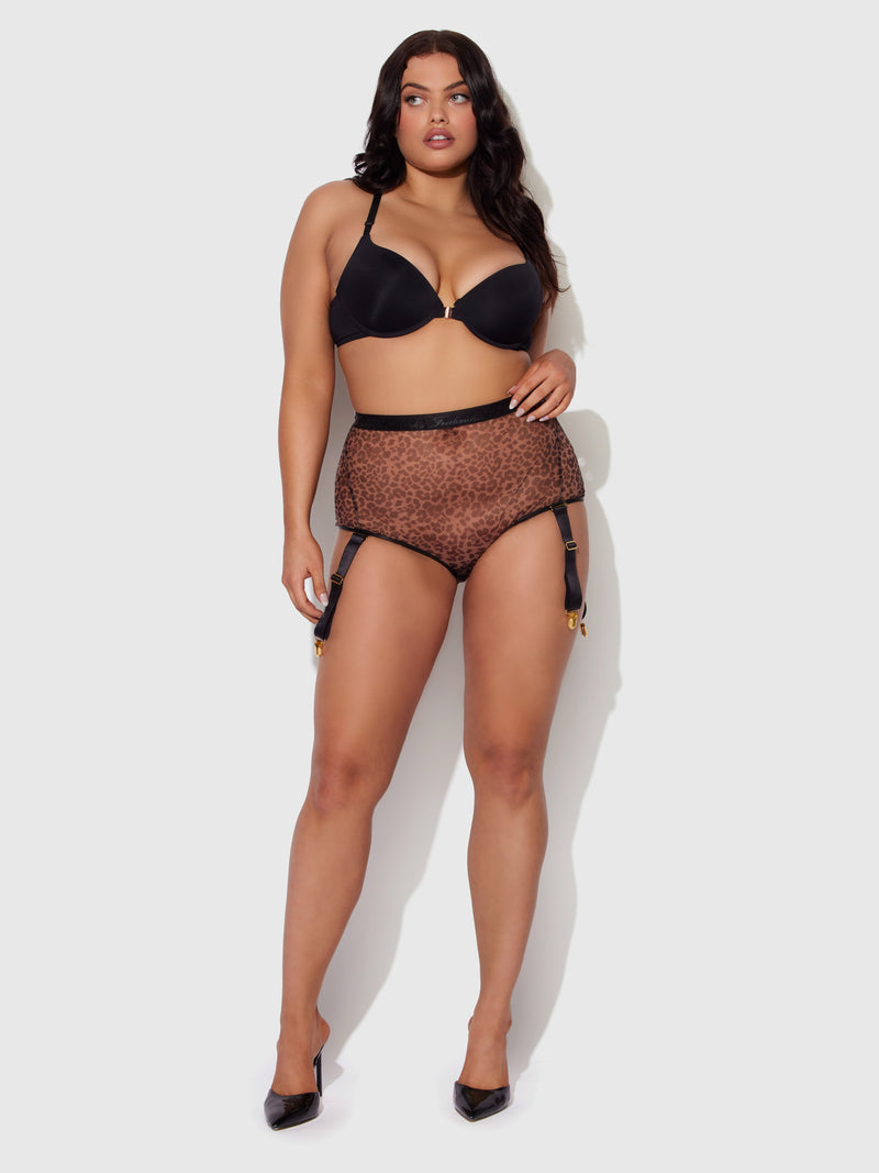 A woman poses confidently against a light background, wearing Frederick's of Hollywood's Pia Mesh Cutout bra and High-Waist Garter Panty in leopard print, paired with matching underwear and black heels.