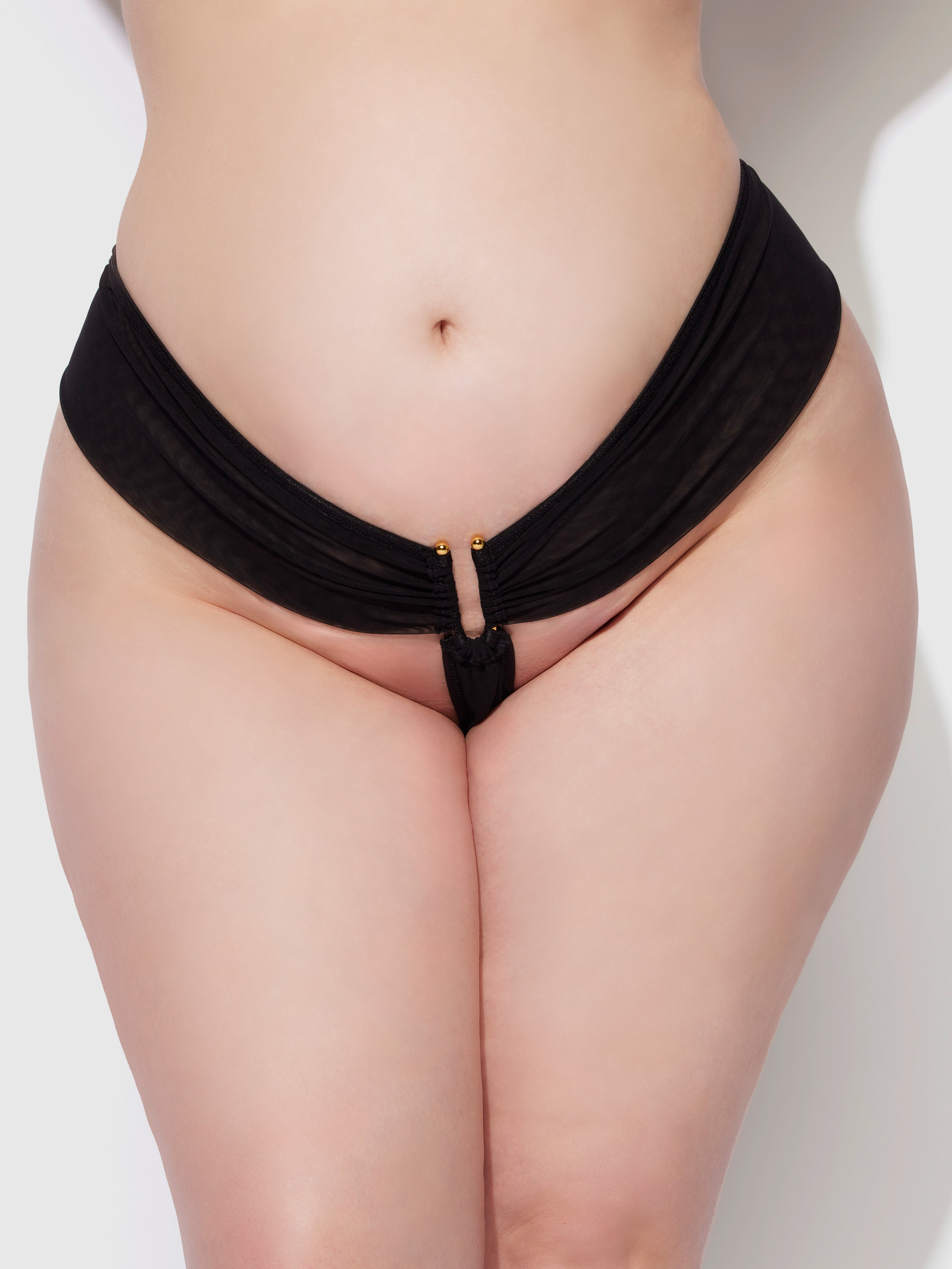 A close-up of a person wearing the Frederick's of Hollywood Alanza Ultra Fine Mesh Hardware Thong, featuring gold accents and a removable gusset, highlights their curves against a plain light background.