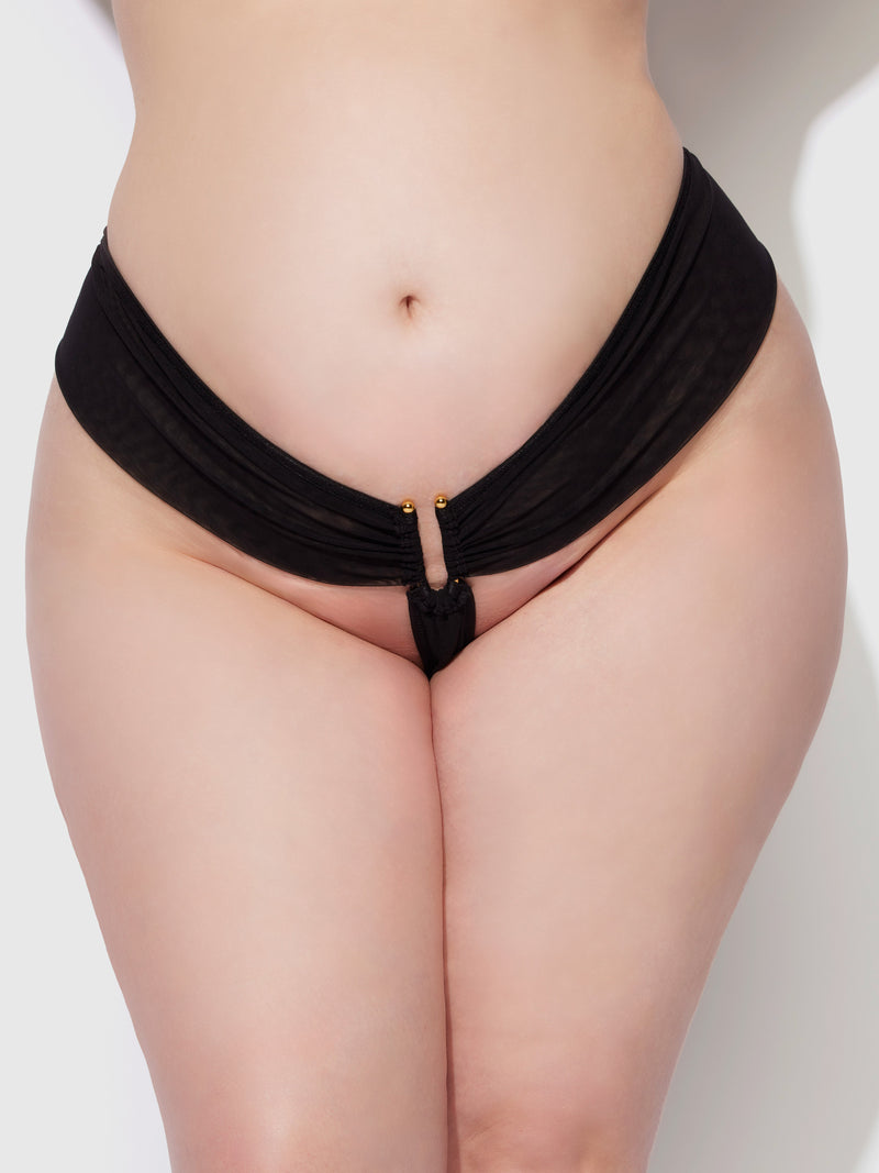 A close-up of a person wearing the Frederick's of Hollywood Alanza Ultra Fine Mesh Hardware Thong, featuring gold accents and a removable gusset, highlights their curves against a plain light background.