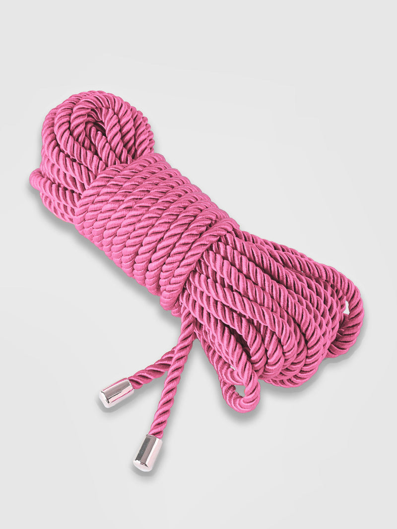 A neatly coiled bundle of Nadya Bondage Rope by Frederick's of Hollywood, featuring pink silky strands with silver metal caps on the ends, is displayed against a plain white background.