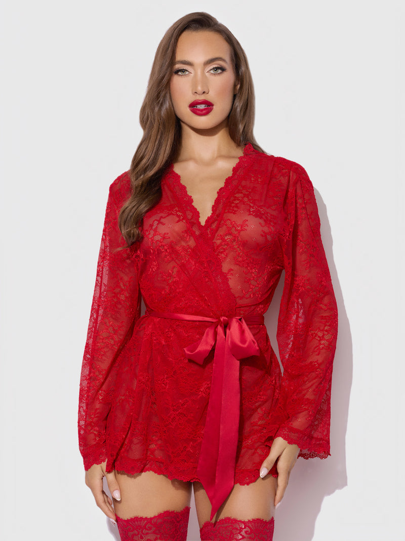 A woman models the Frederick’s of Hollywood Marilyn Monroe Lace Short Robe & G-String Set, featuring a sheer red lace robe with a satin belt, paired with matching red lace stockings and bold red lipstick, standing against a plain light background.
