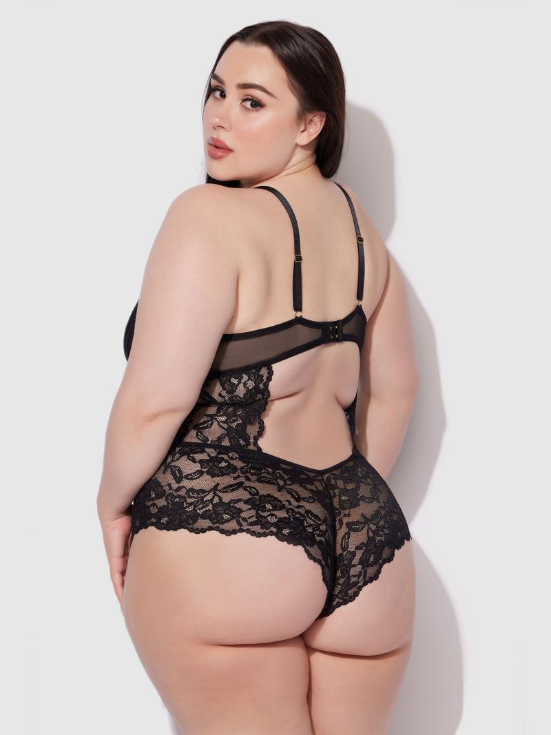 A woman with long dark hair poses with her back to the camera, modeling the Mabel Wireless Teddy by Frederick's of Hollywood. She looks over her shoulder against a plain light background.