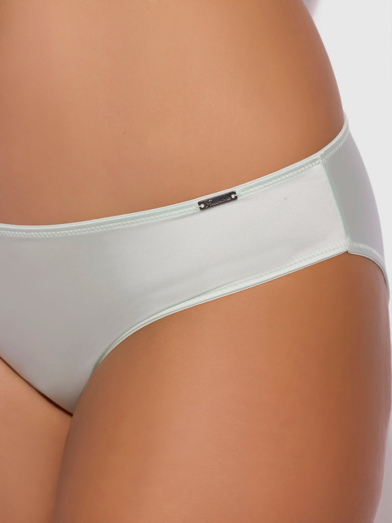 Close-up of a person wearing the Lexi Liquid Satin Hipster by Frederick's of Hollywood, featuring a small rectangular metal tag on the waistband. The panty is light-colored and set against a plain white background.