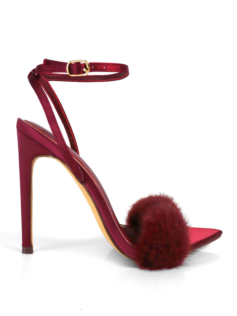 The Aileen Pointed Toe Heel by Frederick's of Hollywood features a deep red shade, ankle strap with gold buckle, maroon pom-pom accent, and pointed heel—offering timeless elegance against a crisp white background.