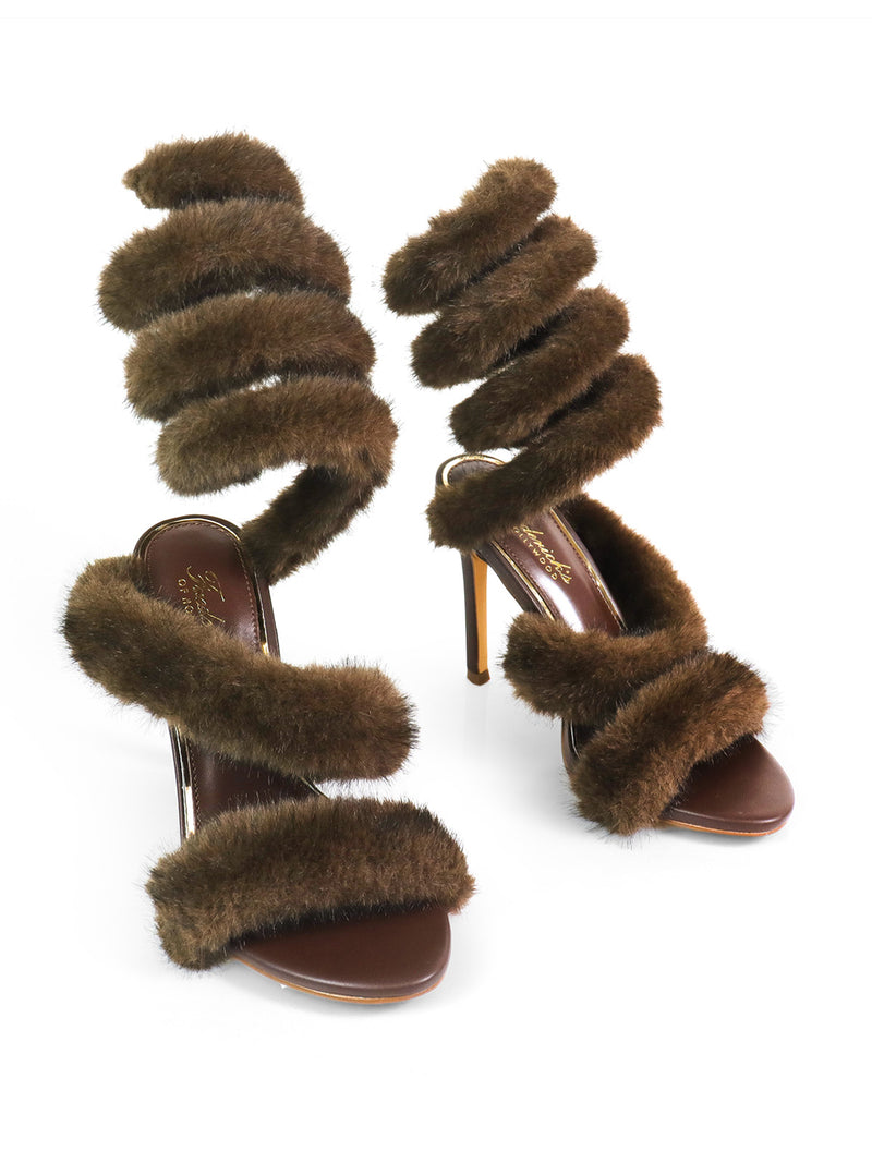 The Allure Fluffy Stiletto Sandal by Frederick's of Hollywood features multiple brown faux fur spiral straps winding from toe to above the ankle, offering a glamorous silhouette against a white background.