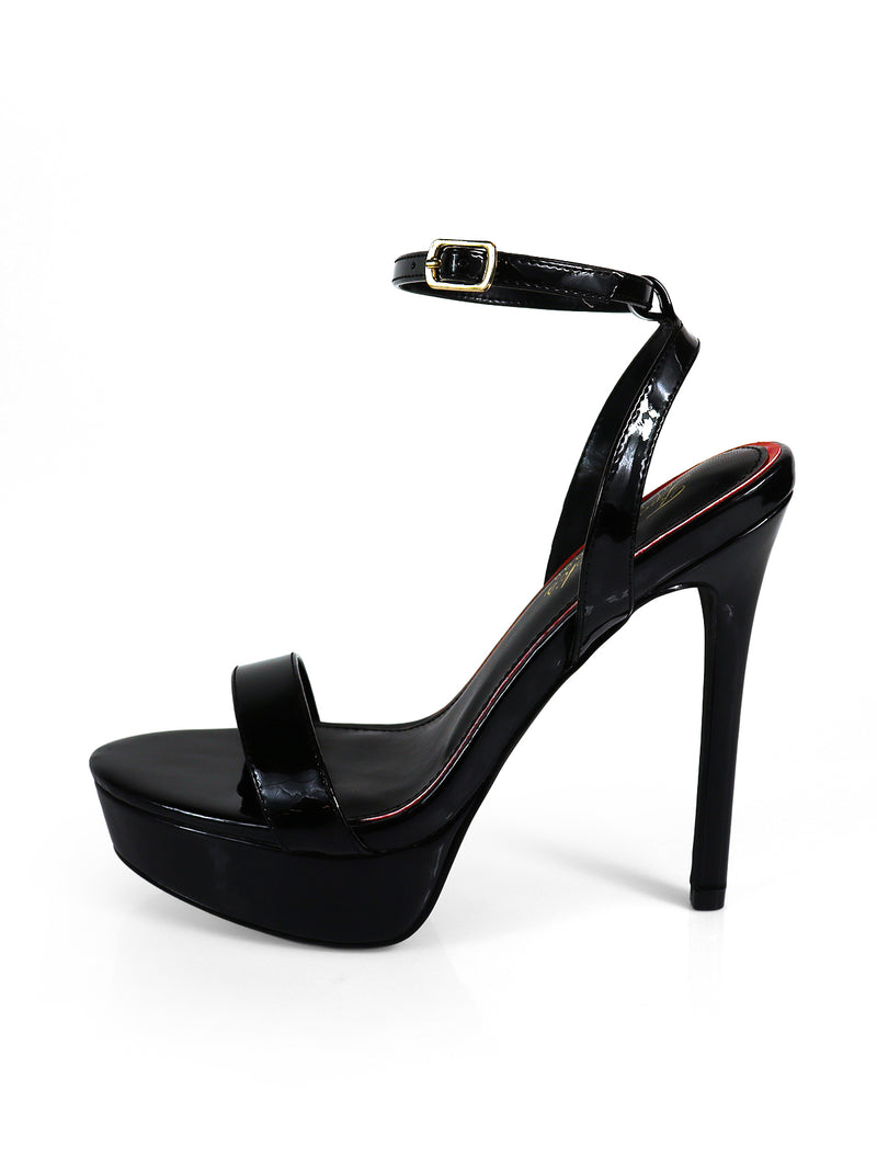The Cupid Strap Platform Heels by Frederick's of Hollywood are black patent leather sandals with a single toe strap and ankle strap with a gold buckle, creating an elevated silhouette against a crisp white background.