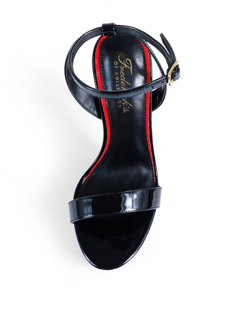 The Cupid Strap Platform Heels by Frederick's of Hollywood are black sandals with high heels, an ankle strap with a gold buckle, and a red and black insole featuring gold text, displayed from above on a white background.
