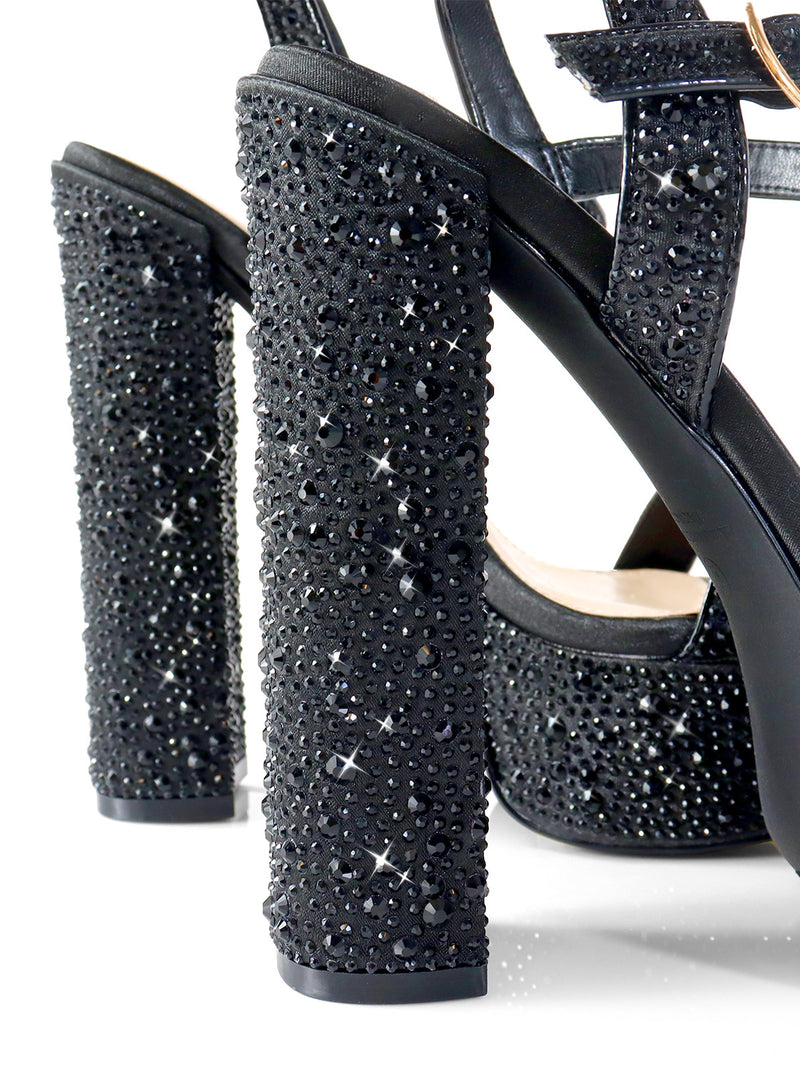 Close-up of the Fabiosa Rhinestone Open Toe Platform Heel by Frederick's of Hollywood, featuring black straps, square heels adorned with sparkling black rhinestones, and a glittery finish—perfect for evening wear.