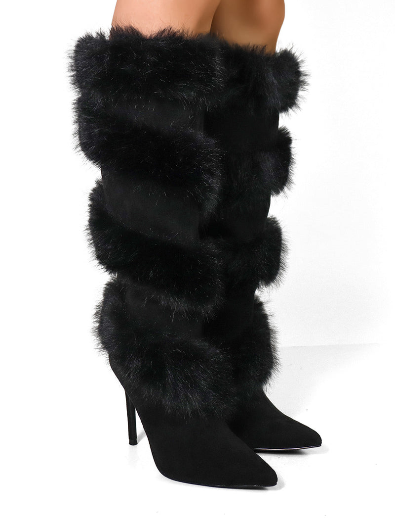 A person stands on a white surface wearing Frederick's of Hollywood Holly Feather Over the Knee High Boots, featuring pointed toes and thick, horizontal bands of black faux fur.