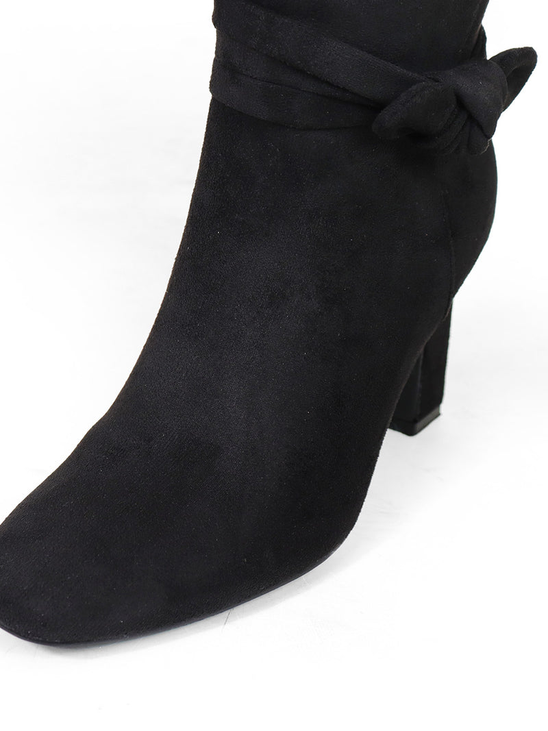 A close-up of the Janeth Ankle Heel Boots by Frederick's of Hollywood, featuring black suede, a chunky heel, and a decorative knot detail bow on the side, photographed against a white background.