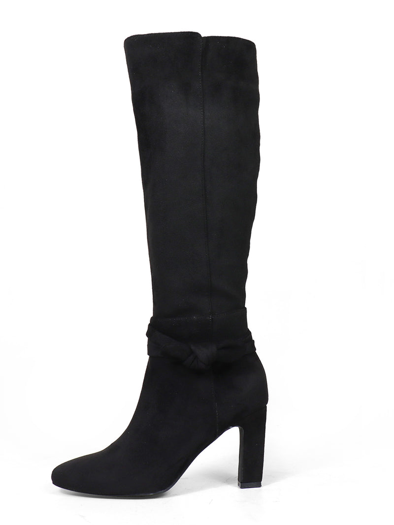 The Frederick's of Hollywood Janeth Ankle Heel Boots are black knee-high suede boots featuring a high chunky heel and a decorative knotted bow detail around the ankle, shown in side profile facing left on a white background—an elegant choice for stylish chunky heel boot lovers.
