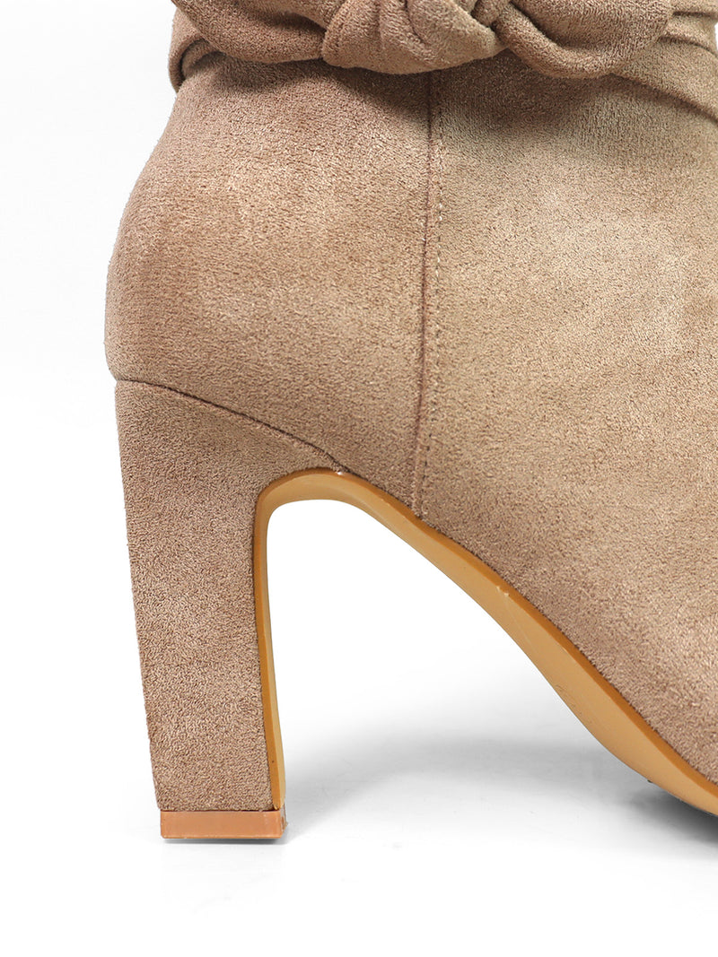 Close-up of the Janeth Ankle Heel Boots by Frederick's of Hollywood, featuring light brown suede, a chunky heel, and a distinctive knot detail near the top edge. The boots have a light tan sole and are set against a plain white background.